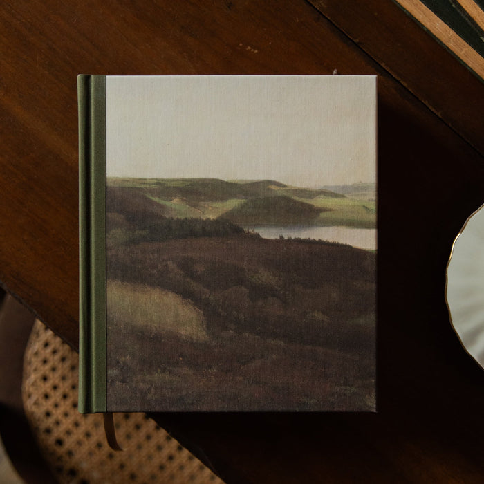 A Bible with a scenic cover on a wooden table next to a cup of coffee