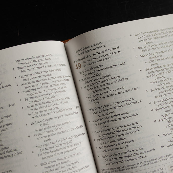 Up close of the top of A leather ESV bible opened to the Psalms pages on a dark wooden table