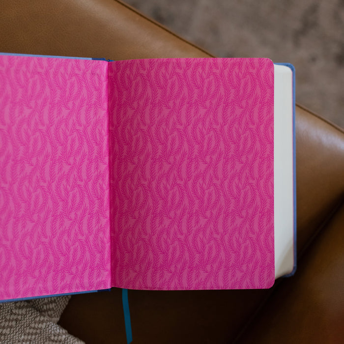 ESV Garden Bible opened to the first page, layered with pink and dark pink leaves while the bible is laying on a leather couch