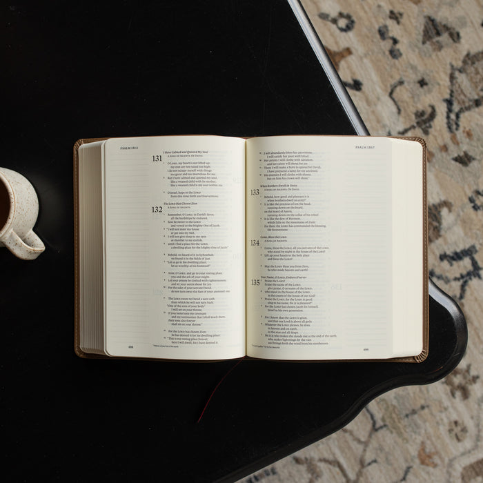 The ESV Single Column Journaling Bible  opened to Psalms 135:7 on a black wooden table near a coffee cup