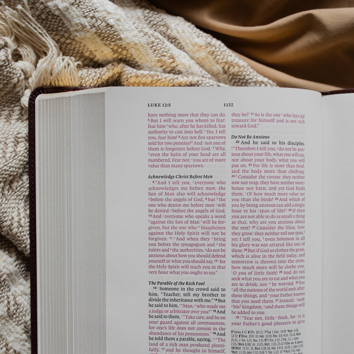 an open leather bible opened to Luke 12:5 on a textured blanket