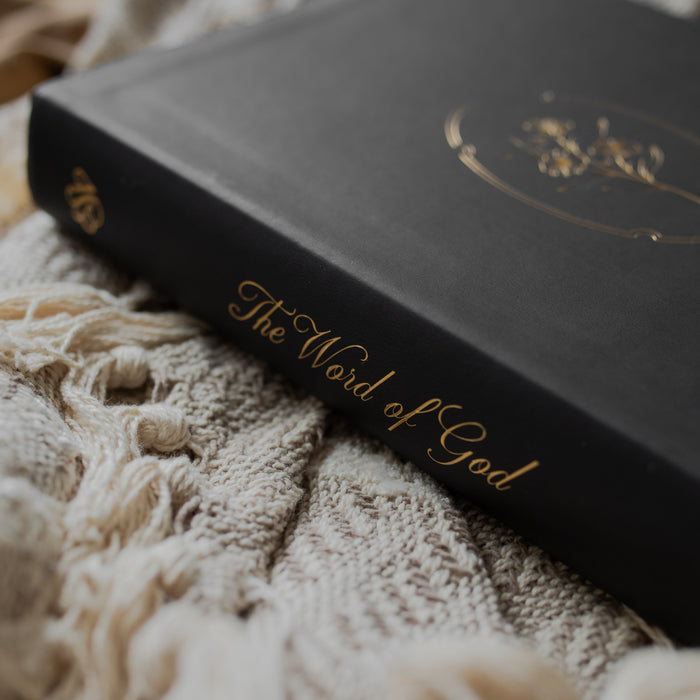 Black bible with gold engraved words on the spine of the bible on a textured blanket