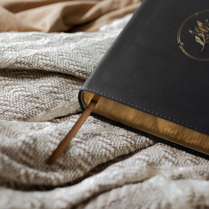 Up close of the black bible with gold engraving and a tassle on a textured blanket