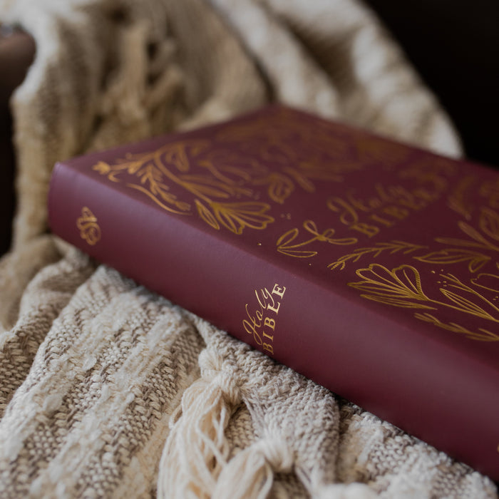 Maroon Bible with gold text on a textured beige blanket