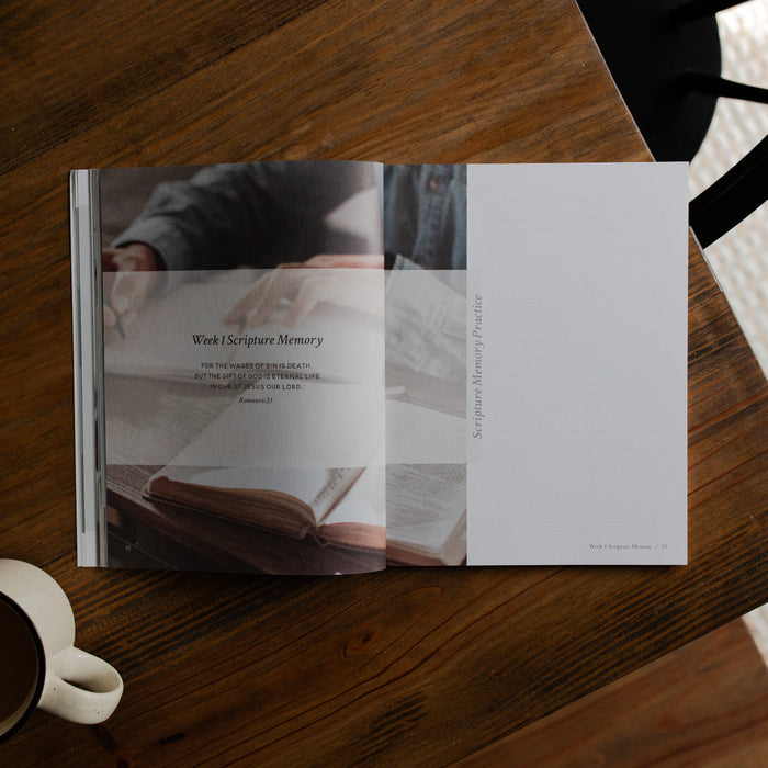 Faith Foundations Mens study opened to the week 1 scripture memory page on a brown wooden table next to a white coffee cup