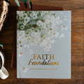 Faith Foundations Matte Study laying on a leather book next to a cup of coffee in a white mug; The study and the coffee is on a brown wooden table next to a hand woven basket