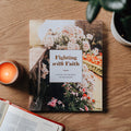 Book titled 'Fighting with Faith' on a wooden table with a candle and plant.