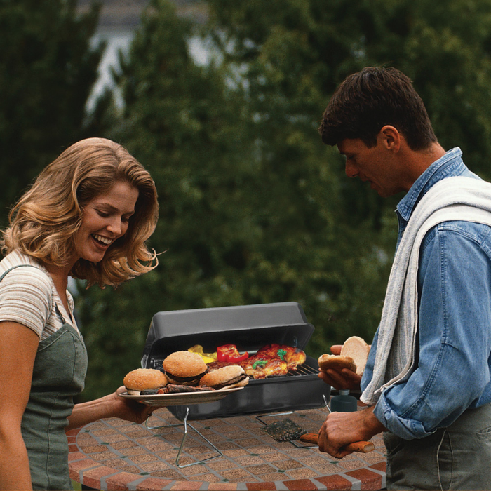 Black electric grill with burgers and vegetables cooking outdoors.