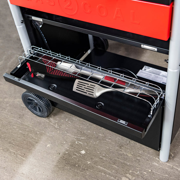 Red and black portable gas grill with charcoal mode, featuring a drawer and wheels.