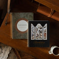 Genesis Spiral and the Revelation Spiral next to each other on a wooden table near a coffee cup
