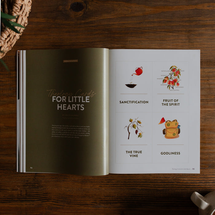 Gospel at Home Issue 8 opened to the theology cards for little hearts Page on a wooden table next to a coffee cup and a woven basket