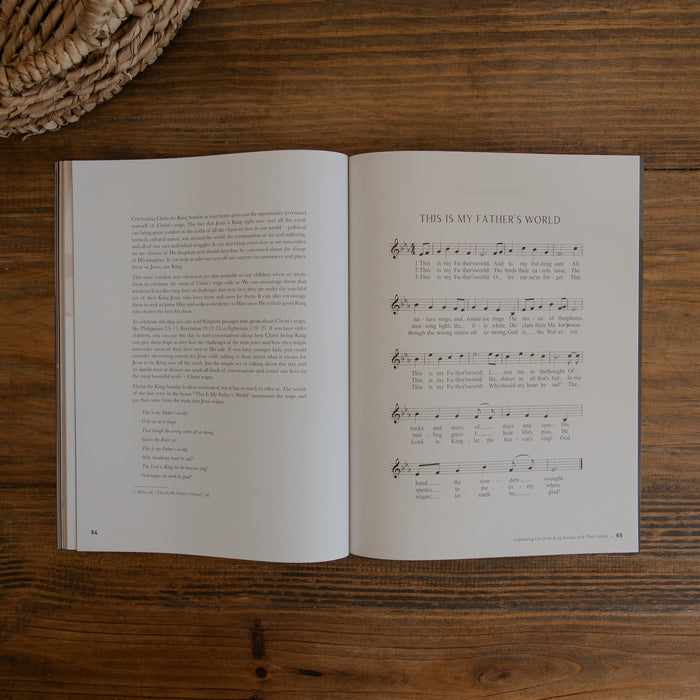 An open magazine laid flat on a wooden table, showing printed text on the left page and sheet music titled 'THIS IS MY FATHER'S WORLD' on the right page. A woven basket edge is visible in the top-left corner.