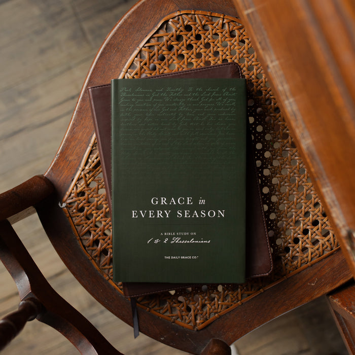 Green book titled 'Grace in Every Season' on a wooden chair with wicker backrest