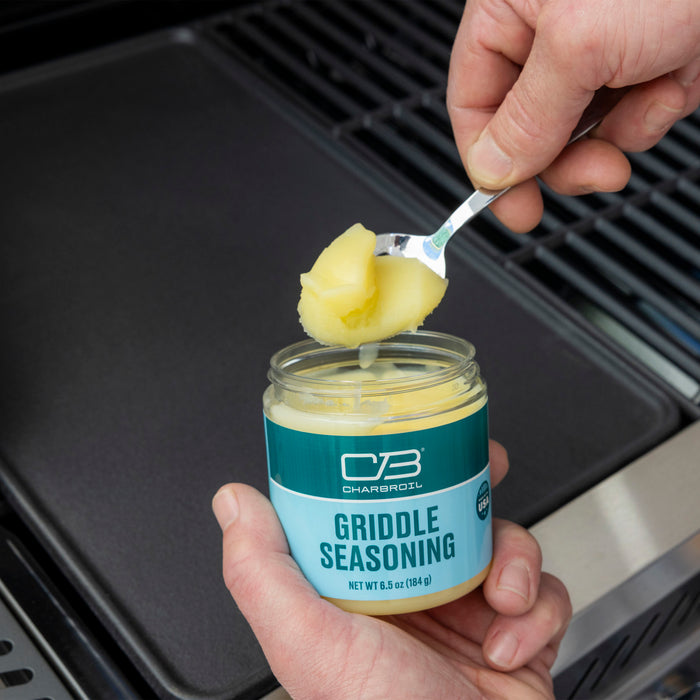 Blue Char-Broil Griddle Seasoning jar, 6.5 oz (184 g), being scooped with a spoon.