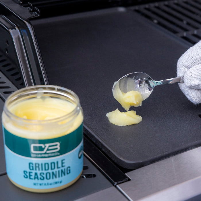 Green CB Griddle Seasoning jar with spoon applying seasoning to griddle.