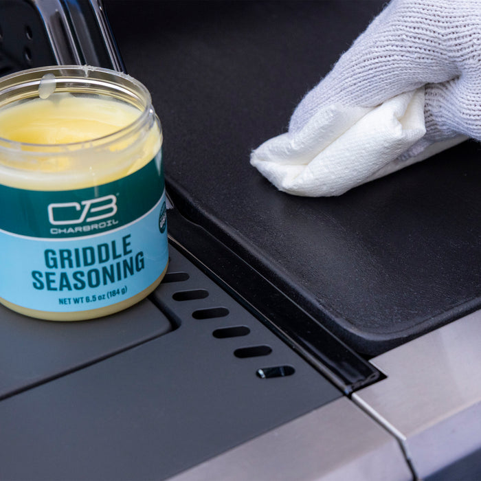 Green Char-Broil Griddle Seasoning jar with white cloth on grill surface.