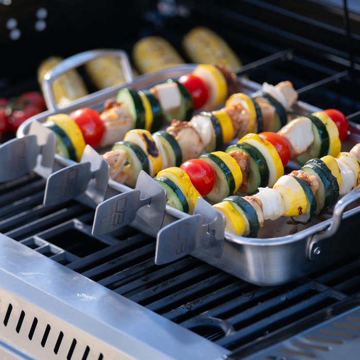 Silver skewer holder with colorful vegetable kabobs on a grill.