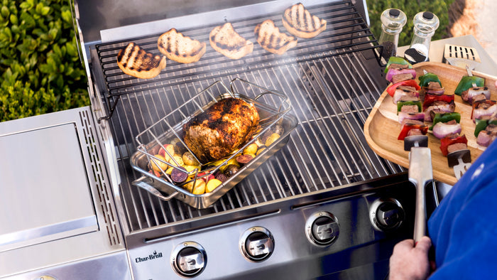 Silver Char-Broil grill with food cooking on grates and skewers nearby.