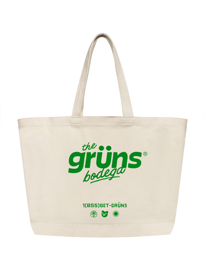 A natural canvas tote bag with long handles features green text reading "the grüns bodega," along with "1(855)GET-GRÜNS" and small icons of a plant, bear, and sun, shown on a white background.