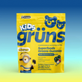 A yellow bag of Kids Grüns Superfoods Greens Gummies in "Bello Banana Berry" flavor features a Minions character on the front, labeled as a dietary supplement for ages 2 to 13 with 28 daily packs, set against a blue-to-yellow gradient background.