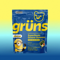 Blue Grüns Superfoods Greens Gummies bag in Bello Banana Berry flavor with Minions branding, on a yellow-to-blue gradient background