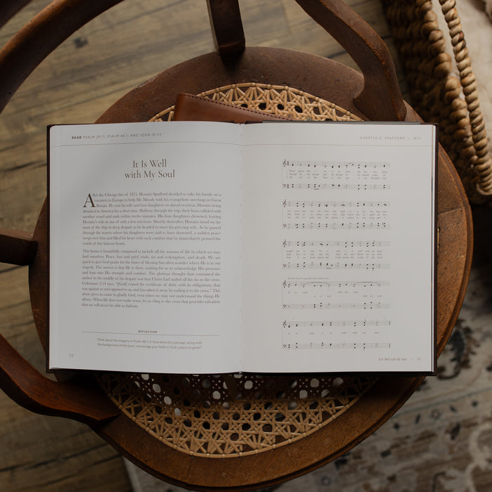 The I need Thee Every Hour book opened to the It Is Well with My Soul page on a wicker chair