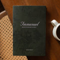 The Immanuel Hardcover cover on a wooden table next to a coffee cup