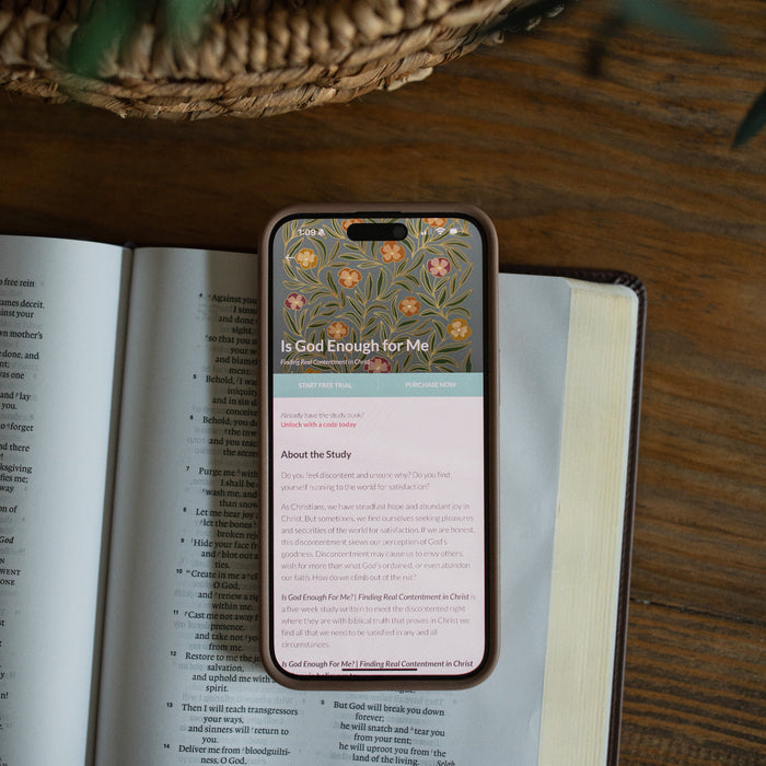 A phone loaded with Is God Enough for Me bible study laying on a open bible on a brown table
