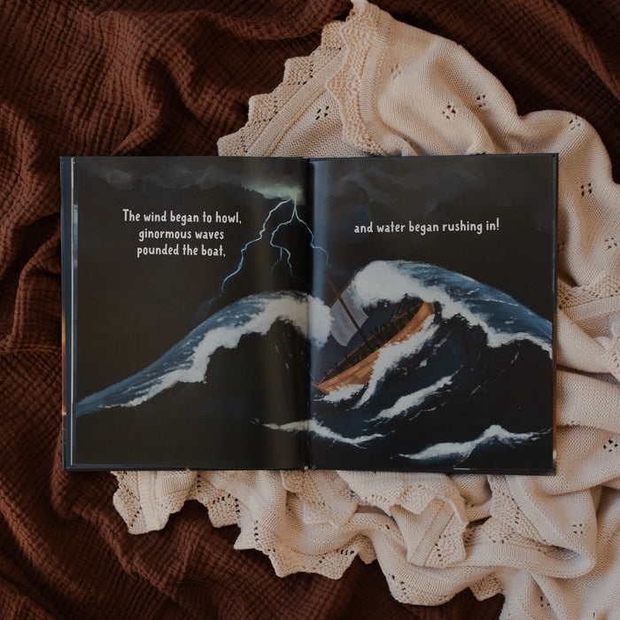 Jesus Calms the Storm Picture Book opened to a boat in the midst of a storm page on a white and brown blanket