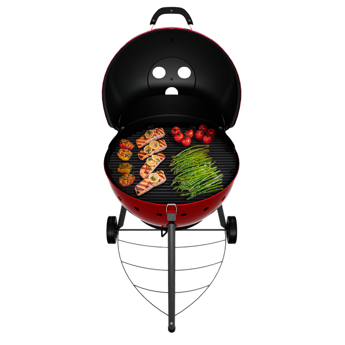Red kettle-style charcoal grill with lid open, cooking salmon, asparagus, tomatoes, and bell peppers.