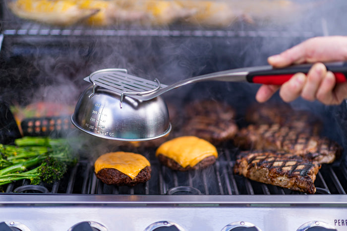 Grill with burgers, cheese, corn, and vegetables cooking.