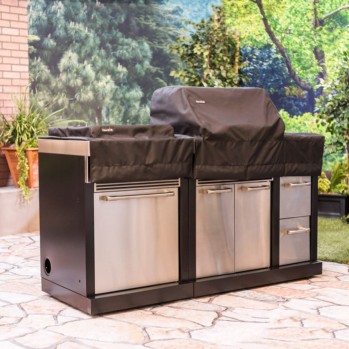 Outdoor grill with black cover and stainless steel drawers on stone patio.