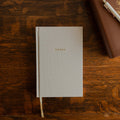 The Notes Lined Journal cover on a wooden table next to a bible with a white pen on it