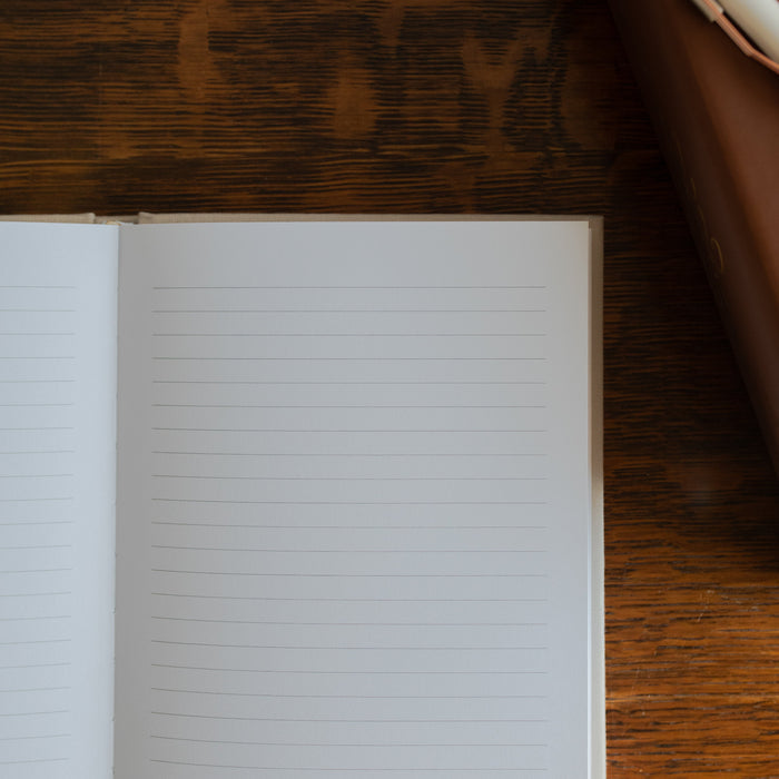Up close of The Notes Lined Journal opened to a blank page on a wooden table next to a bible