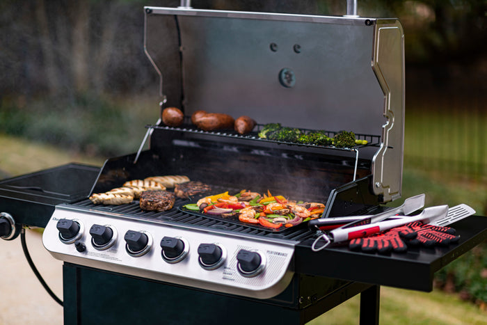 Silver Char-Broil Performance Series gas grill with five burners, cooking assorted food.