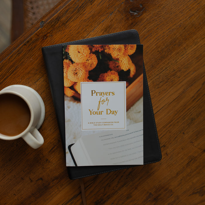 The Prayers for your Day on a black leather bible on a wooden table near a coffee cup
