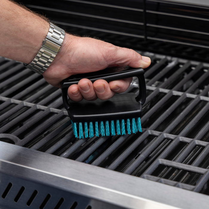 Black grill brush with blue bristles being used on a grill.