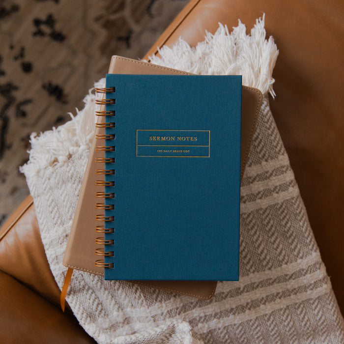 A teal blue spiral-bound notebook labeled 'SERMON NOTES' sits on a cream woven blanket draped over a brown leather chair.