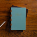 Blue notebook with gold spiral binding on a wooden surface