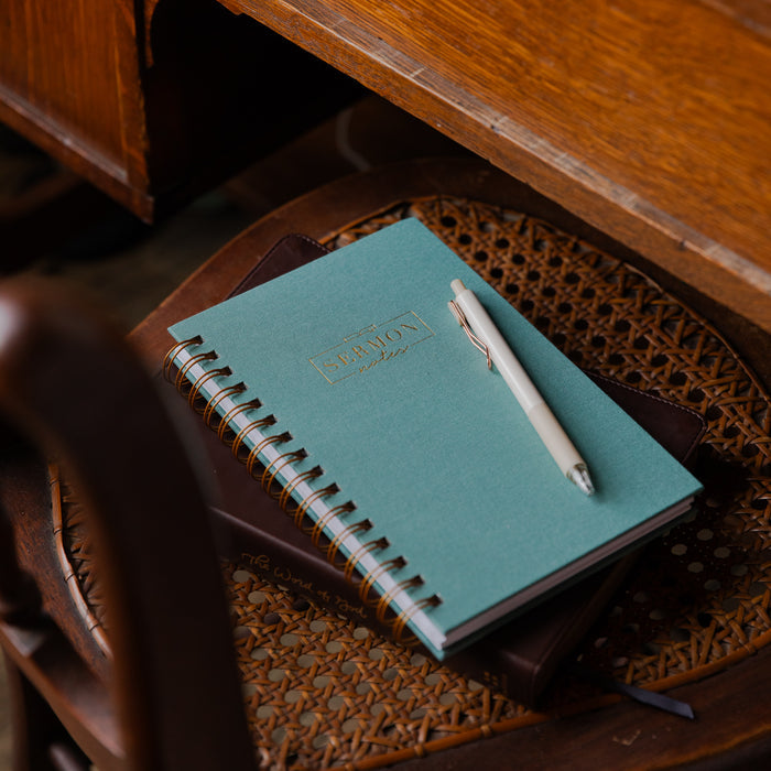 Teal notebook with a pen on a wicker chair next to a wooden desk