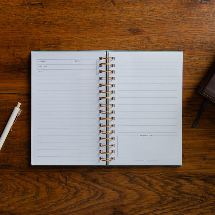 Open spiral-bound notebook on a wooden surface with a pen to the left.