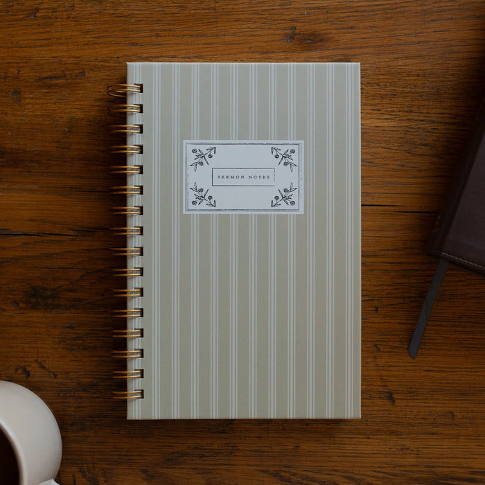 The Sermon Notes Journal with Pale Stripes next to a bible and a coffee cup on a wooden table