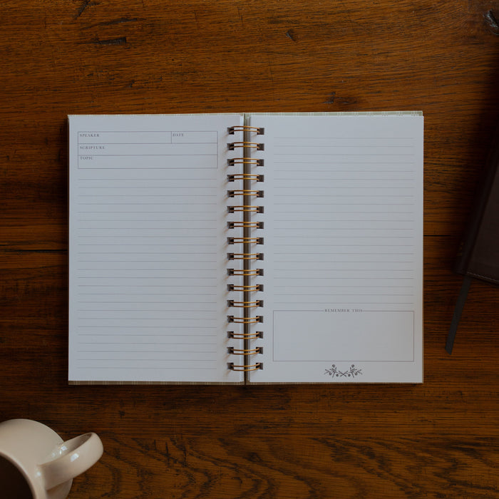 The Sermon Notes Journal with Pale Stripes opened to a blank page next to a bible and a coffee cup on a wooden table
