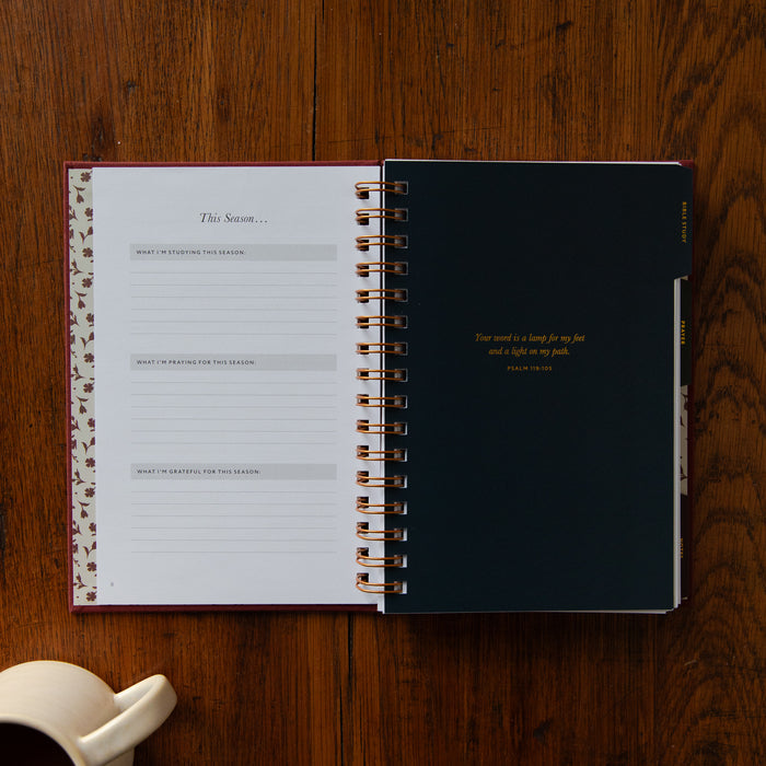 An open spiral-bound journal or planner lies on a wooden tabletop. The left page shows lined sections titled 'This Season.