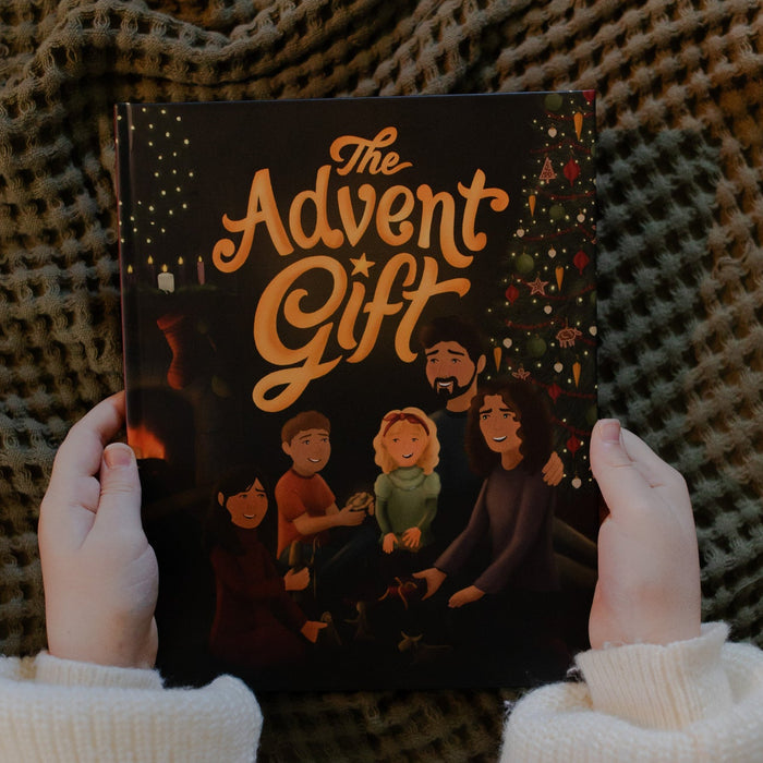 Person holding 'The Advent Gift' book with a checkered fabric blanket