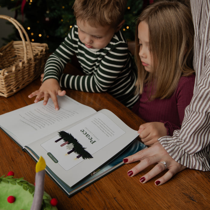 A child and a woman are gathered around a wooden table, reading a book together. The child wears a black and white striped long-sleeve shirt, and the woman wears a brown and white striped blouse.