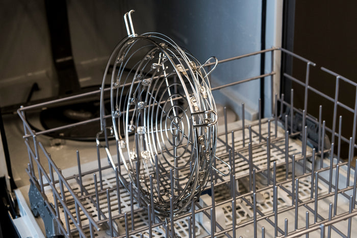 Silver dishwasher rack with adjustable tines and a wire basket for organizing dishes.