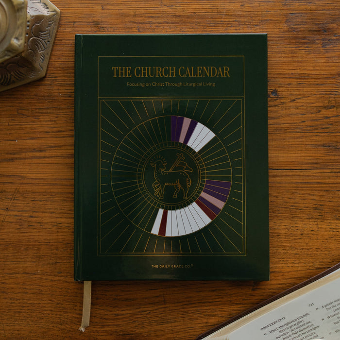 The Church Calendar cover laying on wooden table next an open bible and a bronze candlestick