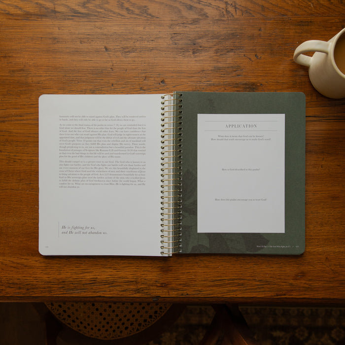 An open spiral-bound booklet or application form book lies on a wooden table. The left page has printed text, and the right page shows a larger document titled APPLICATION.