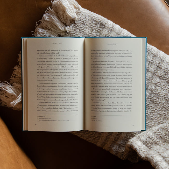 The Pursuit of God opened to page 22 on a cream blanket and leather couch